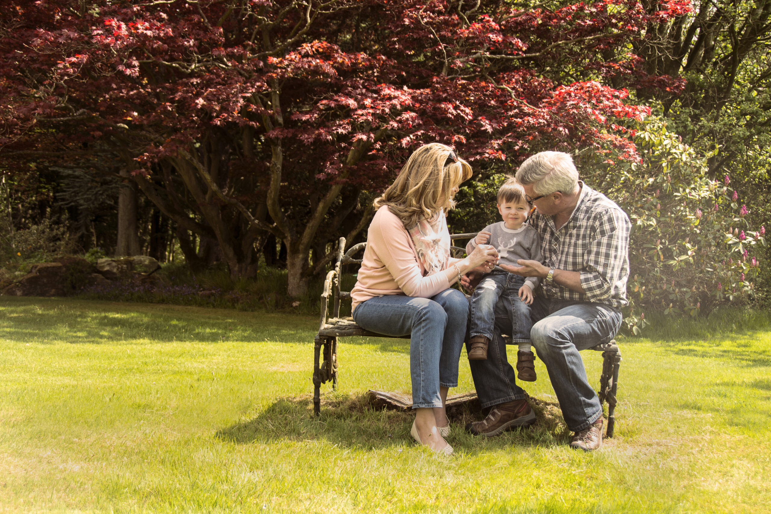 Image of elderly couple with young child sitting on a bench in the sun