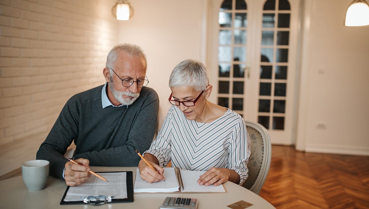 Elderly couple sit down at table and work through documentation